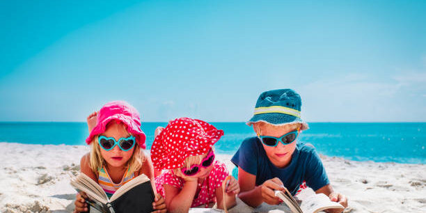 cute happy kids -boy and girls- read books on beach, family vacation concept
